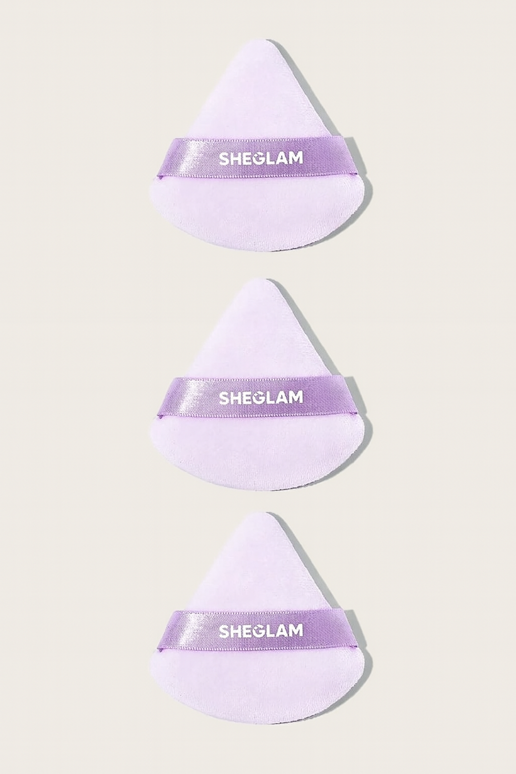 Three purple makeup sponges with 'SHEGLAM' branding on a light beige background