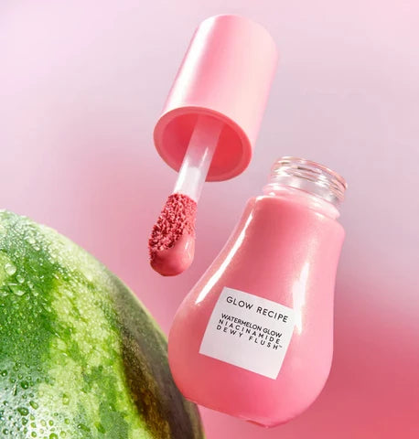 A pink bottle of Glow Recipe watermelon glow activator dent flush with its applicator open, set against a soft pink background with a watermelon slice in the corner.